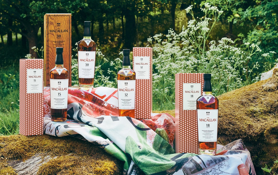 The Macallan Scotch whisky collection display showcasing Harmony Collection and classic Sherry Oak expressions. Premium bottles and matching sustainable packaging boxes arranged on a green fabric backdrop in a natural woodland environment.
